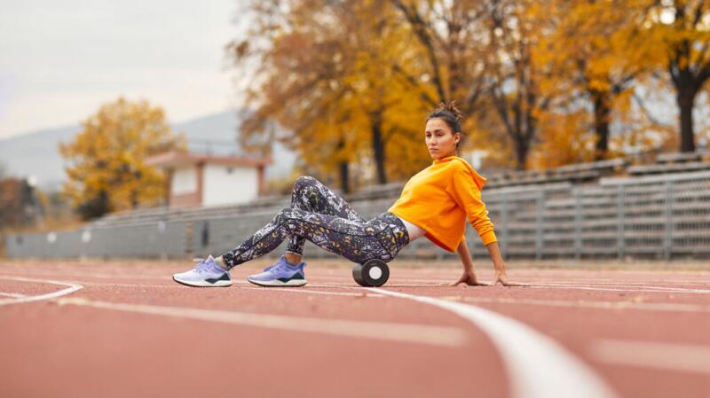 Woman on running track using foam roller under upper thighs