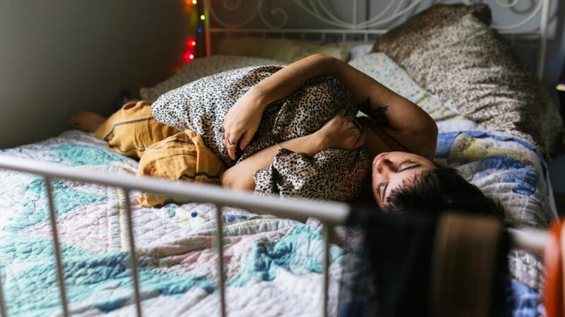 Person curled up with pillow on bed possibly with stomach pain