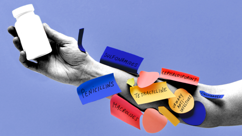 A closeup of a person's arm, with the hand holding a bottle of pills. The arm is covered in sticky notes with the names of the different antibiotic classes on them.