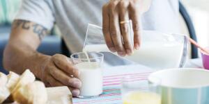 Cropped image of man's hands pouring milk into clear glass