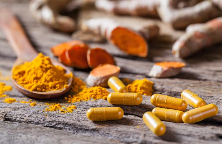 turmeric powder, turmeric capsule and turmeric root on wooden background 