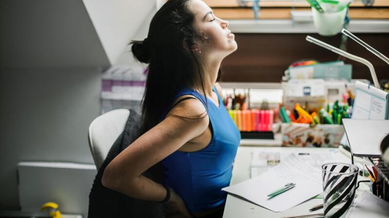 A person is sitting down with their hands on their back.