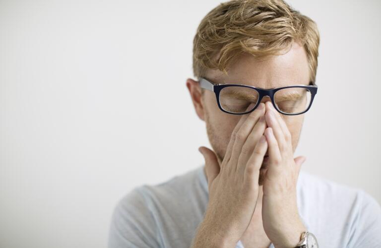 Blonde man rubbing eyes under eyeglasses