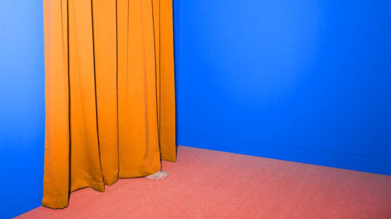 Image of orange curtain on left against blue wall with bare feet sticking out from under the curtain