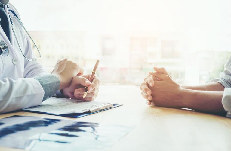 Cropped image of doctor's and patient's hands on desk during conversation