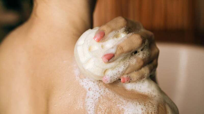 A close-up of someone rubbing soap over their skin in the shower.