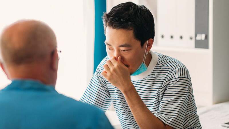 Male holding his nose and speaking with a doctor