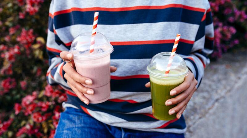 A person holds two milkshakes in clear plastic cups.