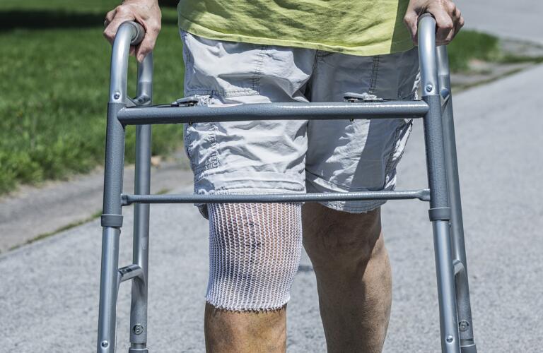 senior adult woman walking slowly and carefully outside with walker after knee replacement