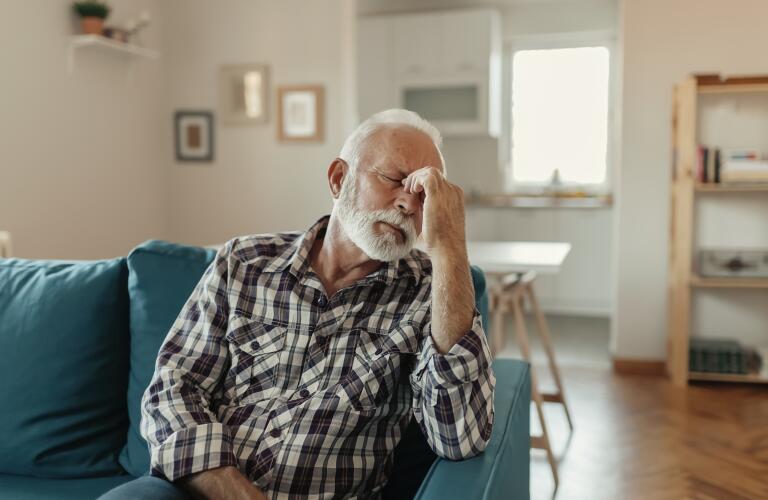 Older man sitting out couch with pain between eyes