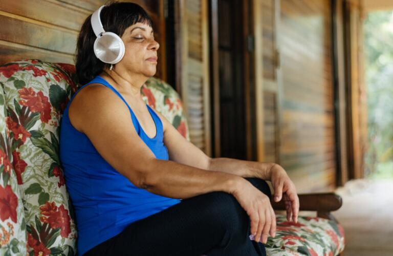 person with eyes closed wearing workout clothes and headphones sitting cross-legged on a bench