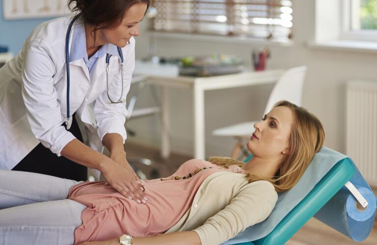 Young female Caucasian patient on exam table with female Caucasian doctor feeling abdomen