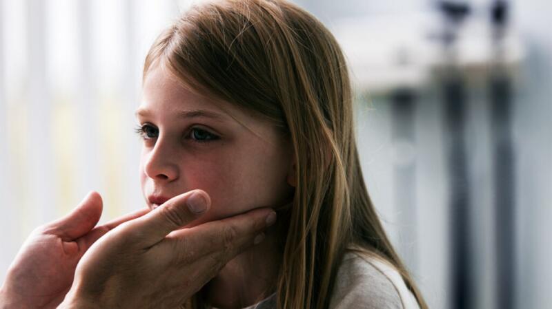 a person is checking the throat of a young girl for swelling