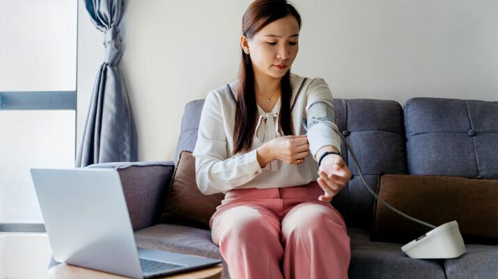 a woman is sat on a sofa measuring her blood pressure