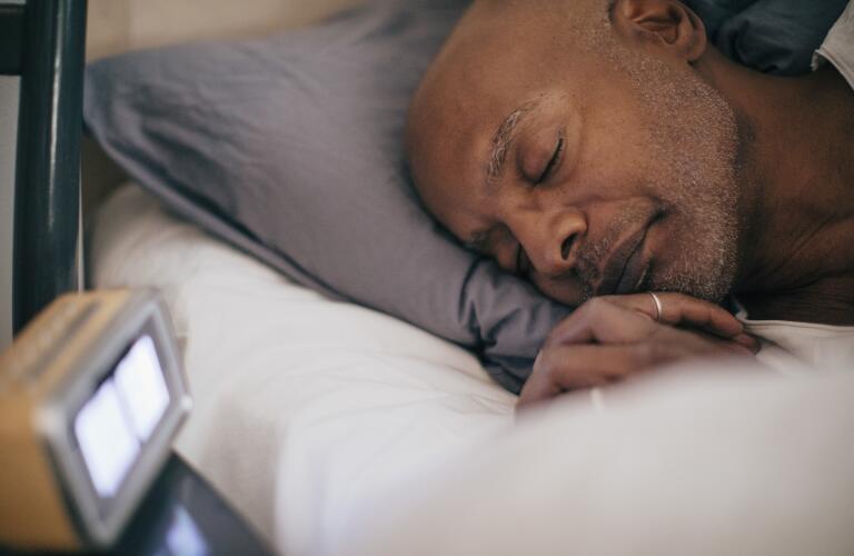 Middle aged man asleep in bed near clock