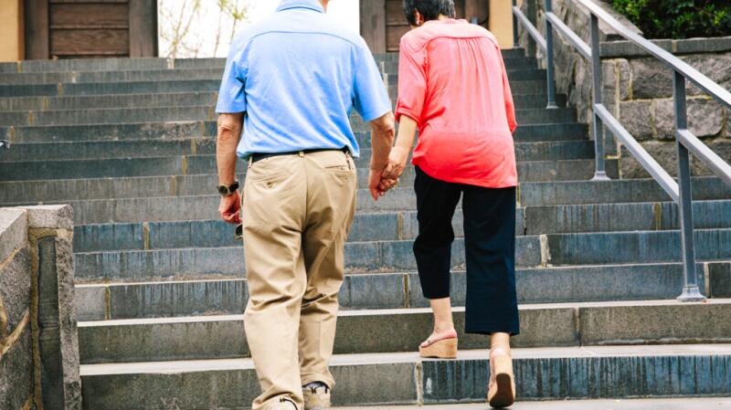 Two older adults climb some steps while holding hands.