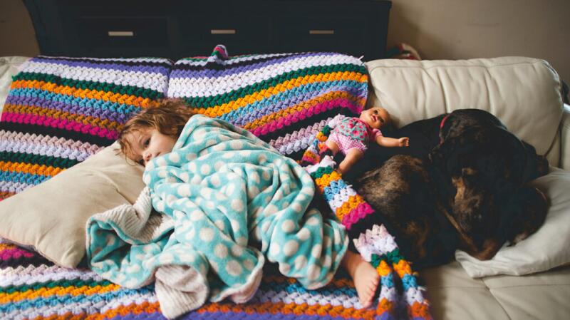 Young girl sick on couch under blanket with toy doll