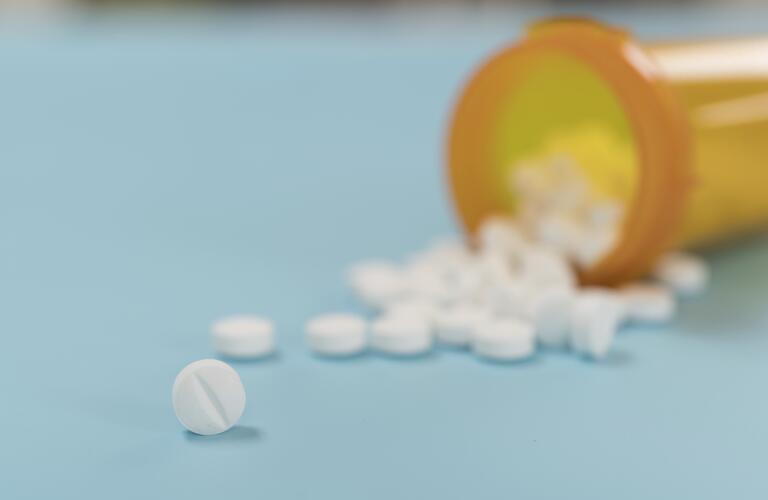 small, white, round tablets spilling from medicine bottle on blue background, closeup