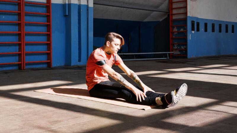 Young man stretching on floor mat with hands on his shins