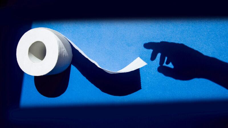 A roll of toilet paper with the shadow of a hand reaching for it