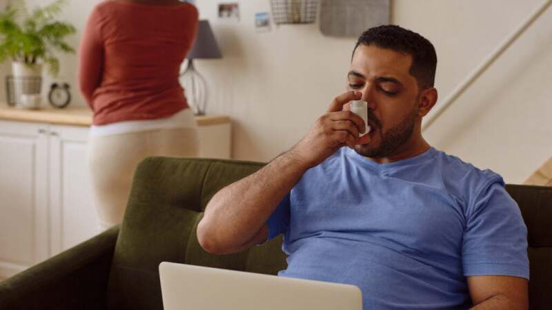 Someone uses an inhaler while sitting and looking at a computer.