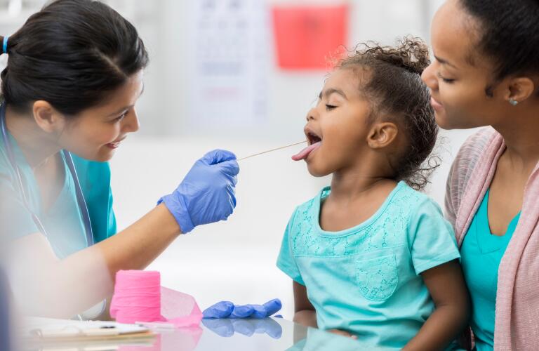 Young African American girl getting throat checked by urgent care nurse or physician assistant