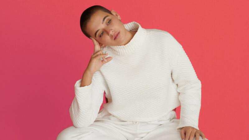 Female sitting in front of a pink background thinking