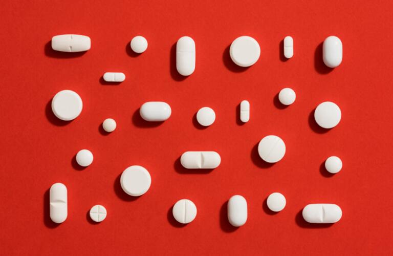 Assorted white pills arranged neatly against solid red background