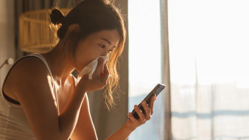 A person is holding a tissue on their nose and looking at their phone.