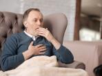 senior man sitting in chair and coughing