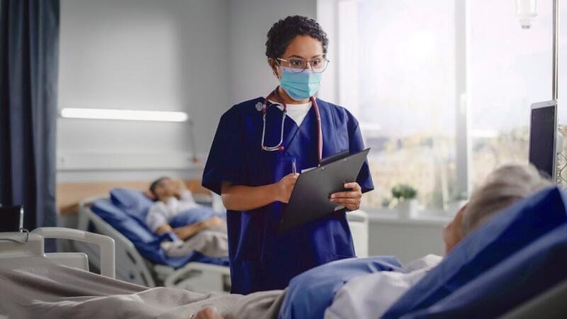 Medical professional wearing a mask talking to patient in hospital room