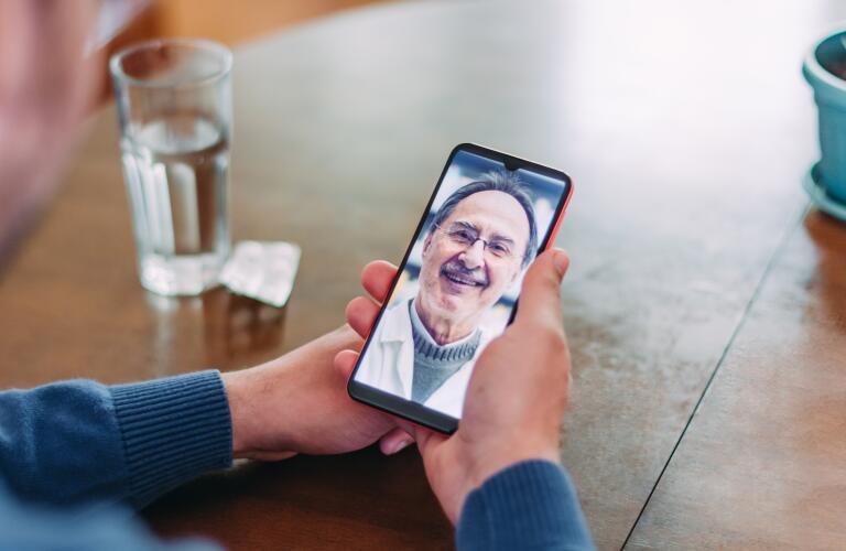 closeup of hands holding smartphone during telehealth appointment on dining table next to glass of water