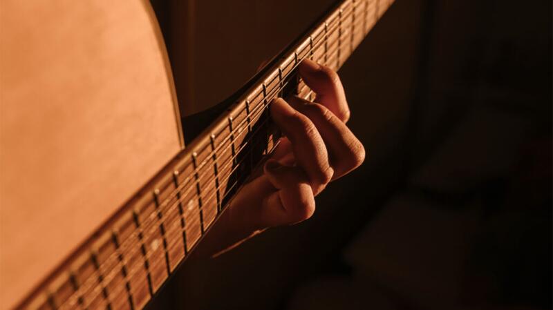 Unseen person playing guitar with fingers on frets
