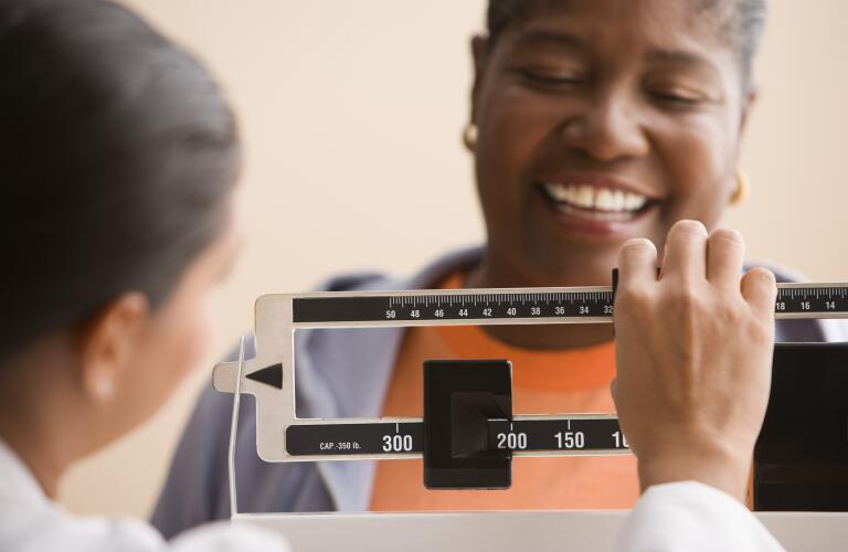 Older African American woman smiling on scale as doctor or nurse checks weight
