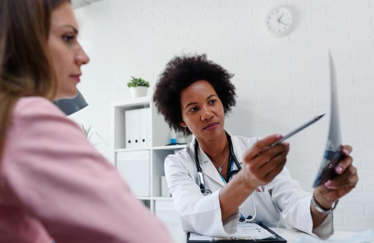 female doctor pointing to x-ray film while talking with female patient at desk in medical office