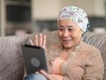senior Asian female cancer patient waving at tablet and sitting on couch during telehealth appointment