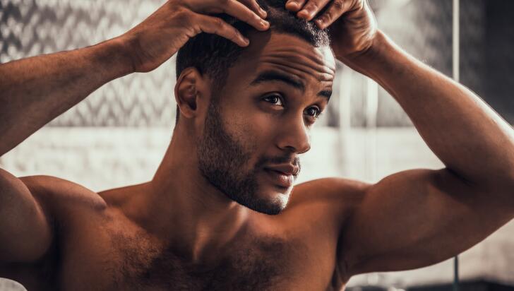Young African American man checking hair and scalp in bathroom mirror