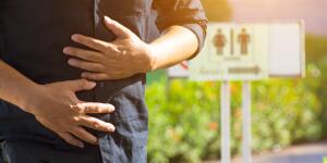 young Caucasian man holding stomach with restroom sign in background