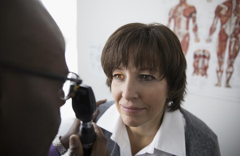 male African American eye doctor examining eyes of middle aged female Caucasian female