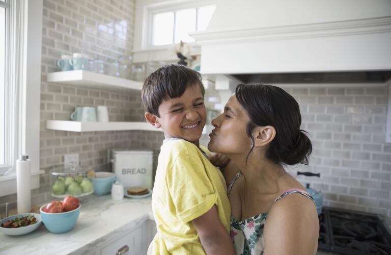 playful mother holding and kissing son in kitchen