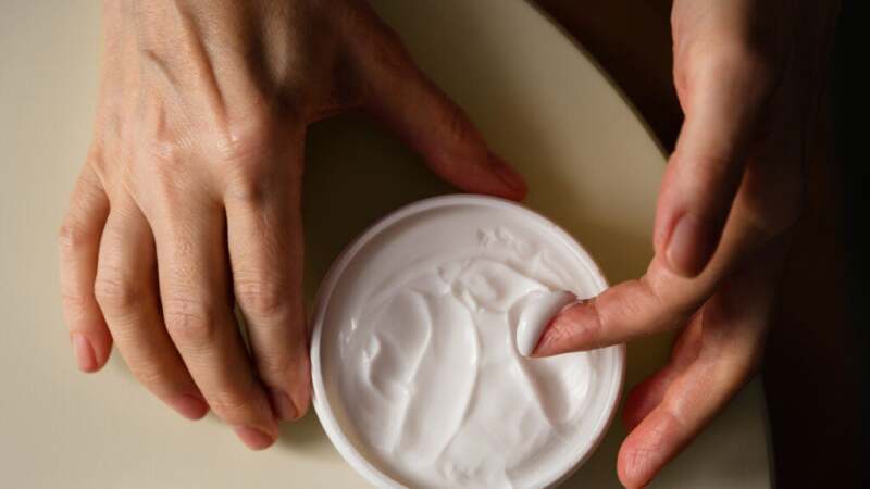 A person dipping their finger into a jar of skin cream