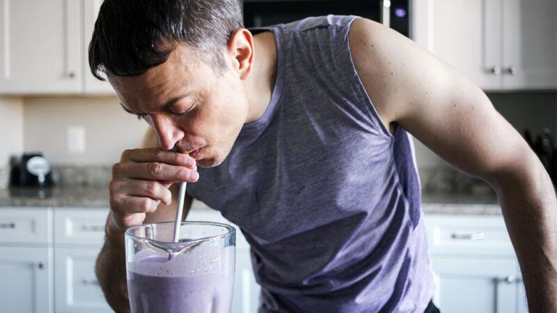 Someone drinks a smoothie from a blender with a straw.