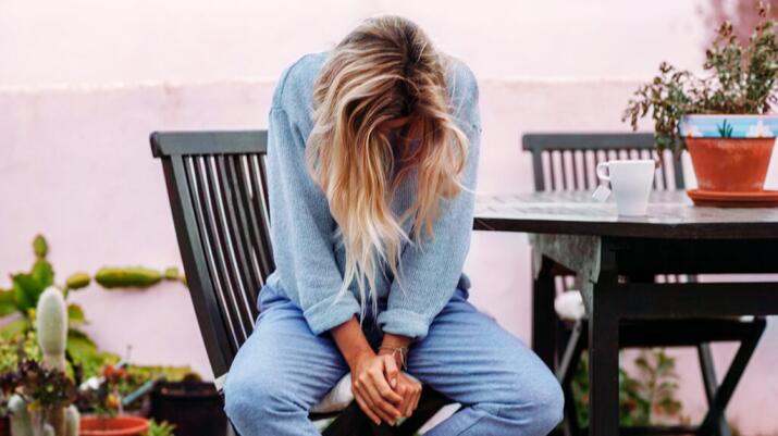 A woman sits on a chair and bends her head down.
