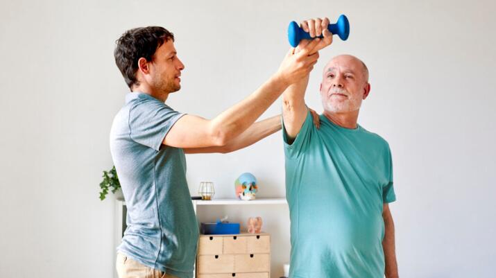 Older man in physical therapy lifting hand weight with arm extended