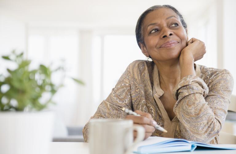 senior woman sitting at table thinking and writing