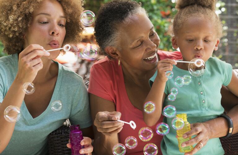 Mother, grandmother and granddaughter blowing bubbles together