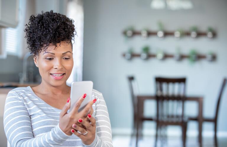 African American woman in her 30s looks at mobile phone at home