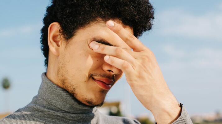 young man outside rubbing his eyes 