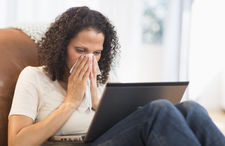 Portrait of woman sitting with laptop and blowing nose
