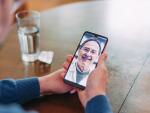 closeup of hands holding smartphone during telehealth appointment on dining table next to glass of water